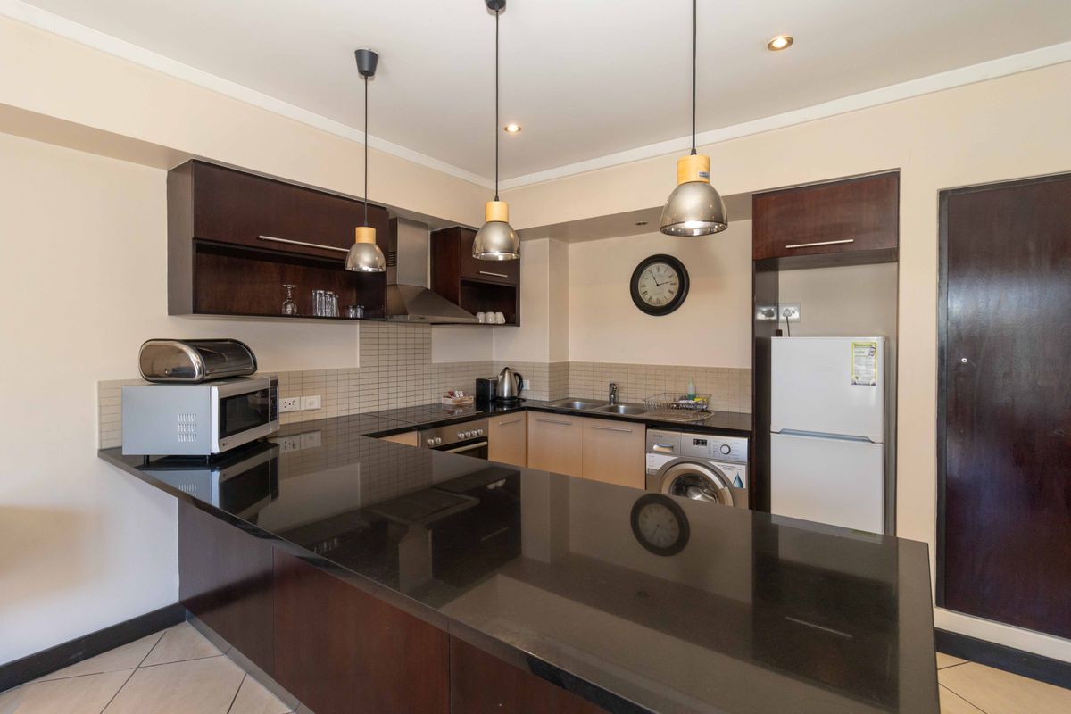 A functional kitchen featuring dark wood cabinetry, a black granite breakfast bar, tiled backsplash, and integrated stainless steel appliances.