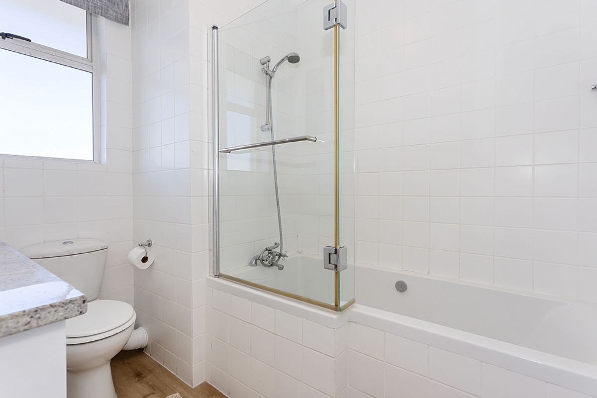 A functional bathroom featuring a white bathtub with a glass shower screen, a toilet, and tiled walls.