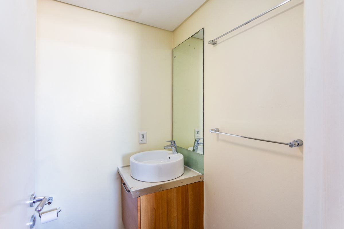 A compact bathroom featuring a modern vessel sink, vanity cabinet, wall-mounted mirror, and chrome towel rails.