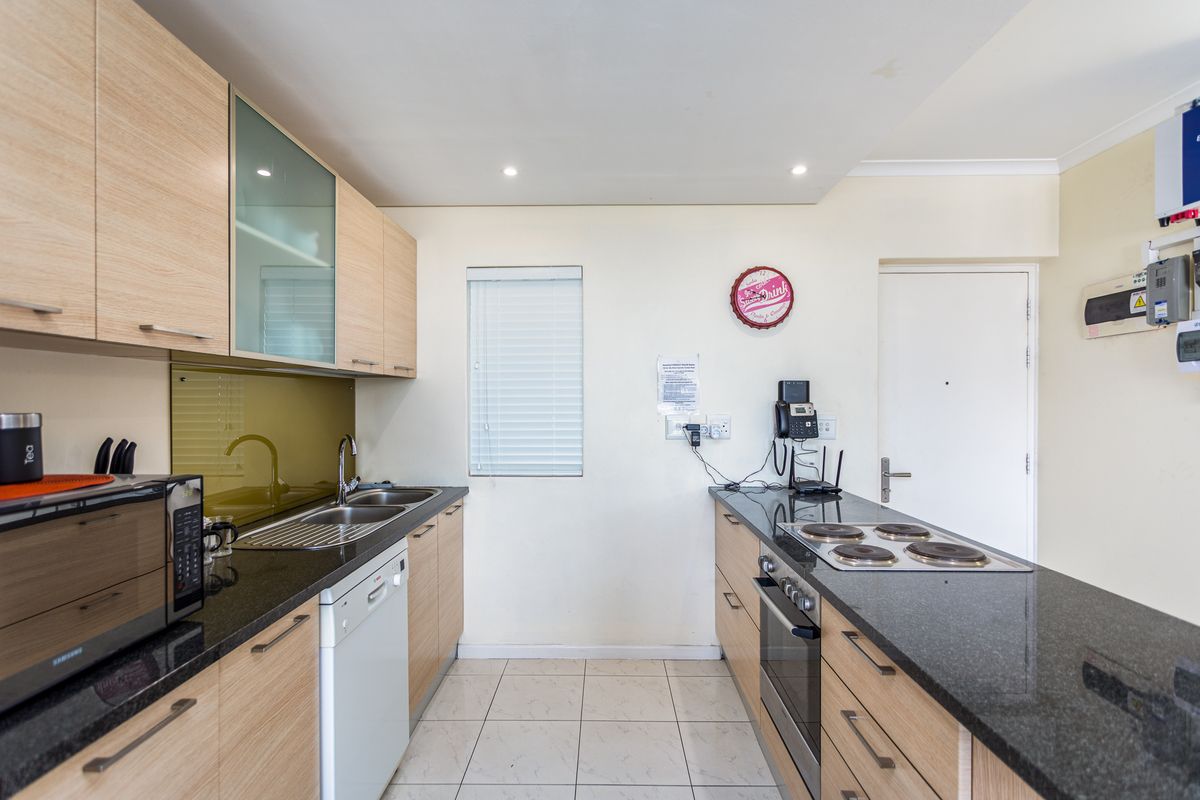 A functional kitchen featuring light wood cabinetry, dark granite countertops, a built-in oven, electric hob, and a stainless steel sink with a glass splashback.