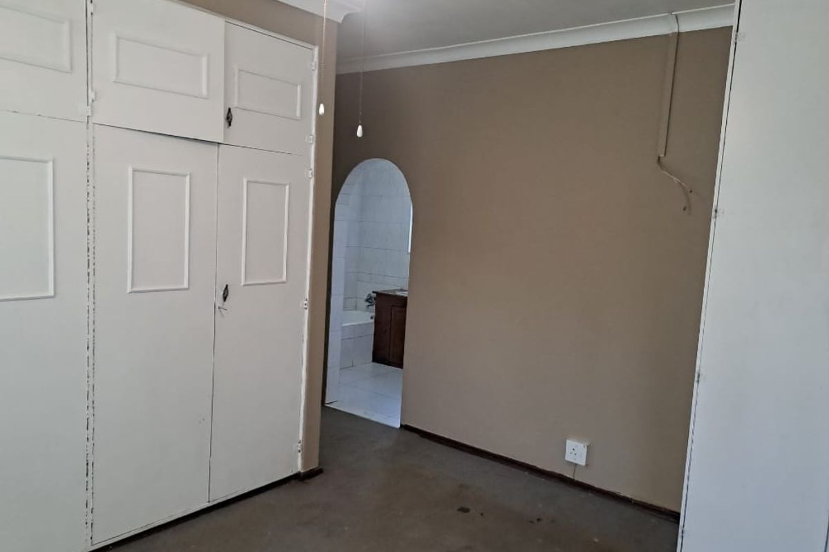 A bedroom featuring built-in cupboards and an arched doorway leading to an en-suite bathroom, requiring cosmetic updates to flooring and wall finishes.