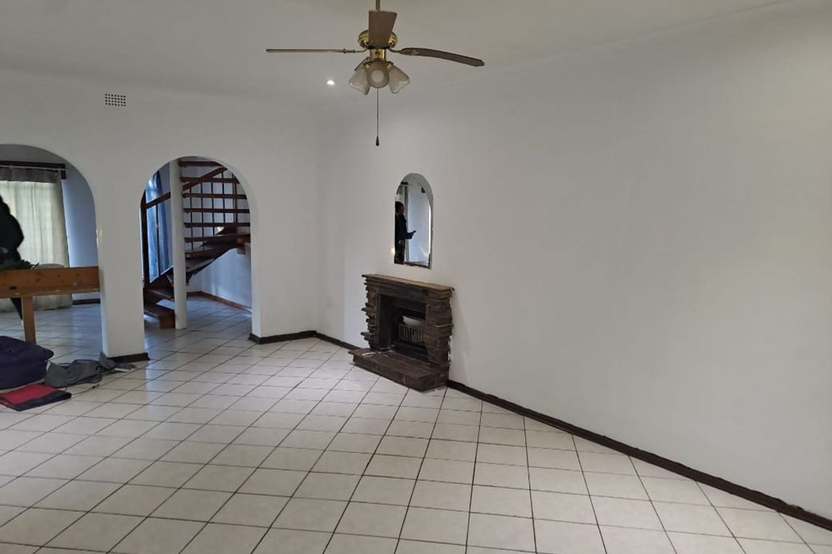 Spacious living area featuring tiled flooring, a built-in stone fireplace, and an arched entryway leading to a wooden staircase.