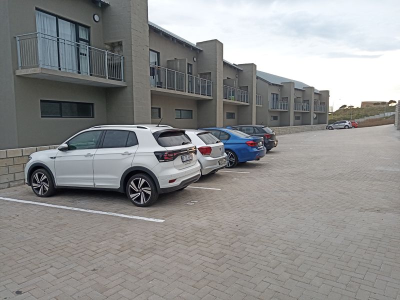 Exterior view of an apartment complex featuring a paved parking area and multiple units with private balconies.
