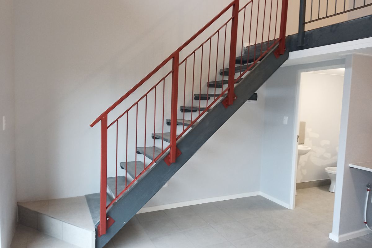 Open plan living area featuring a modern industrial-style metal staircase with red balustrades, leading to a mezzanine level with adjacent bathroom access.