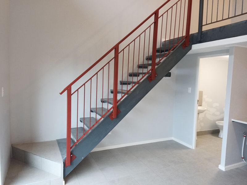 Open plan living area featuring a modern industrial-style metal staircase with red balustrades, leading to a mezzanine level with adjacent bathroom access.