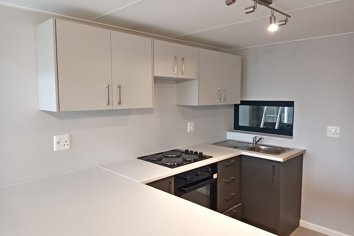 A clean, modern kitchen featuring neutral cabinetry, built-in electric oven and hob, stainless steel sink, and functional track lighting.