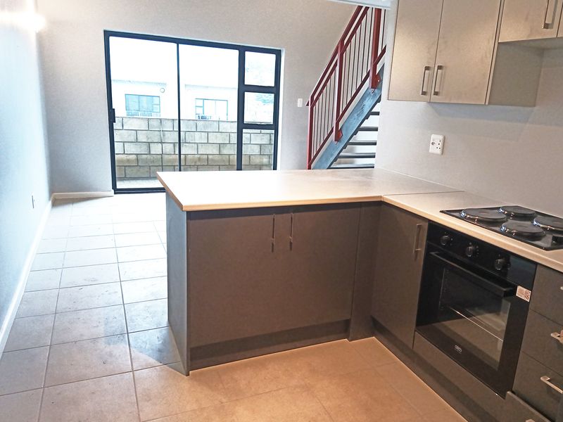 Open-plan kitchen and living area featuring modern cabinetry, built-in oven, tiled flooring, and direct access to an outdoor space via sliding glass doors.