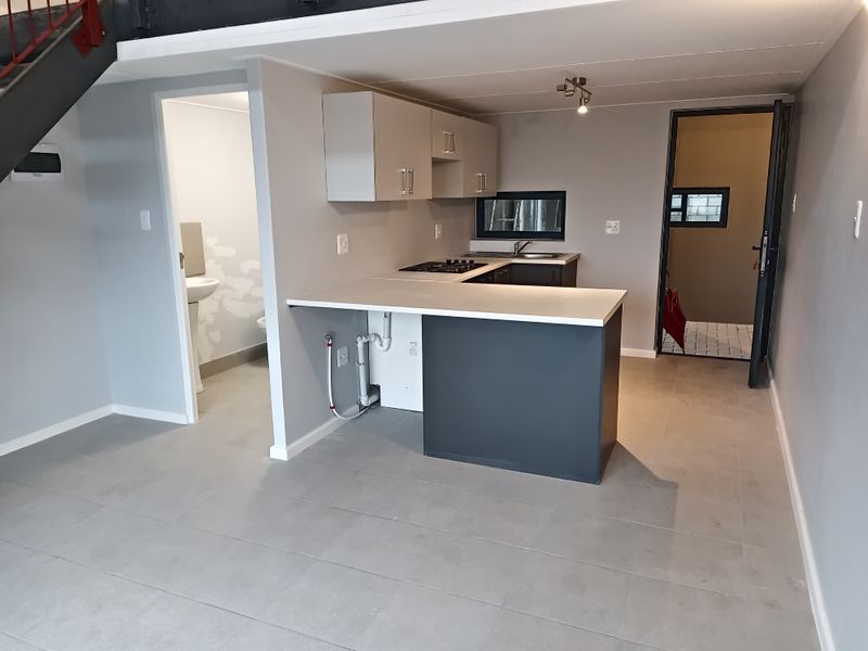 Open-plan kitchen and living area featuring tiled floors, built-in cabinetry, gas hob, and a breakfast counter, with an adjacent bathroom and staircase.