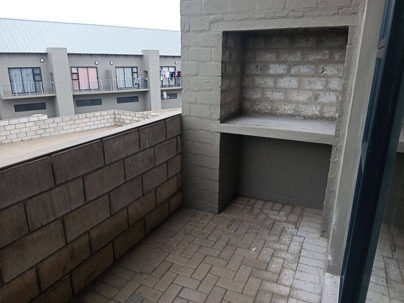 A balcony featuring a built-in braai area with unfinished masonry walls and brick paving, offering an outdoor space for potential improvement.