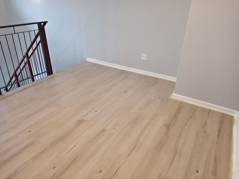 A bright, empty landing area featuring light wood-look laminate flooring and a modern metal staircase railing.