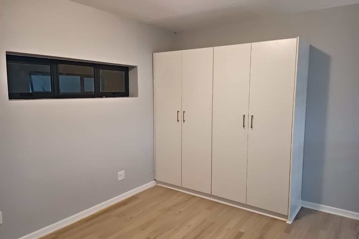 A clean, empty bedroom featuring light-toned laminate flooring, neutral grey walls, and a large white built-in wardrobe.