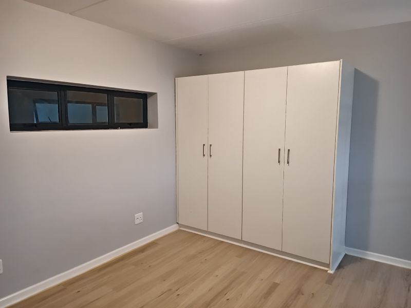 A clean, empty bedroom featuring light-toned laminate flooring, neutral grey walls, and a large white built-in wardrobe.