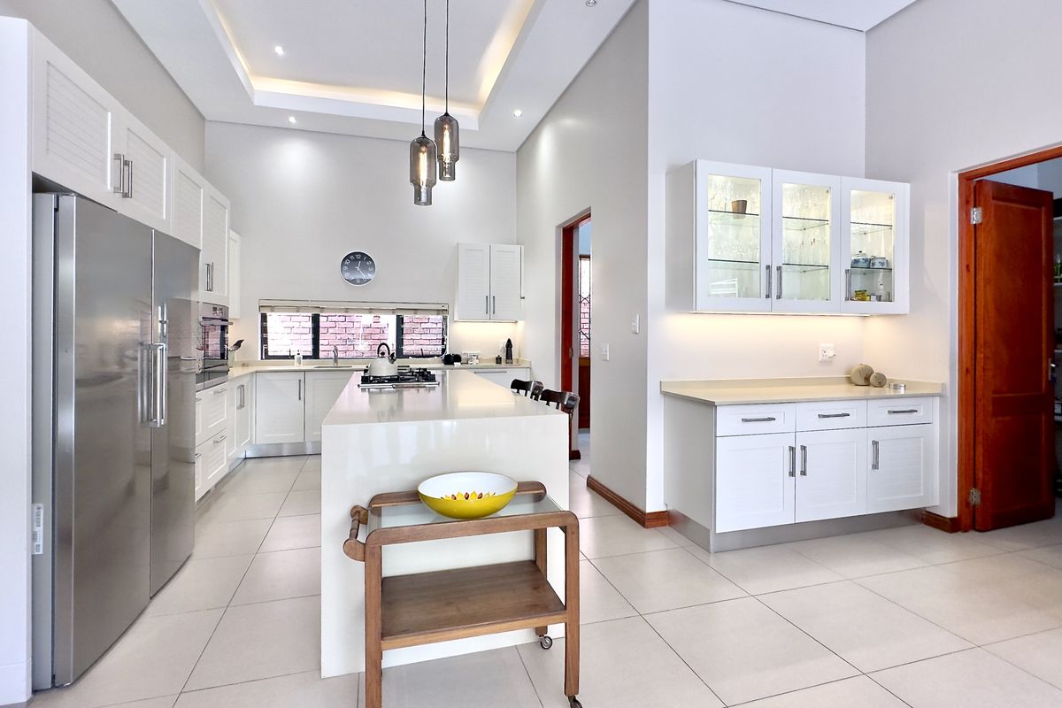 Modern kitchen featuring white cabinetry, stone countertops, a central island with a built-in hob, recessed ceiling lighting, and an adjacent scullery area.