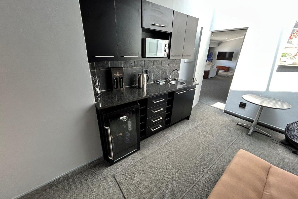 A compact kitchenette featuring dark cabinetry, granite countertops, a built-in microwave, and a small under-counter beverage fridge.