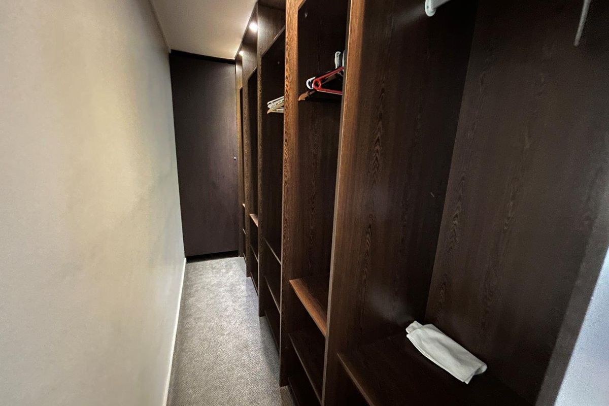 A walk-in closet featuring dark wood built-in cabinetry with integrated shelving and hanging rails, finished with carpeted flooring.