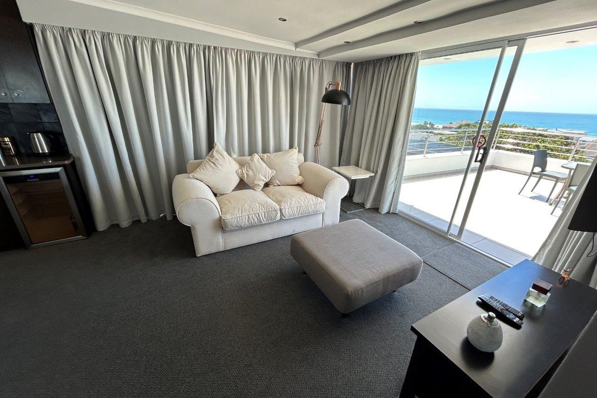 A comfortable living area featuring wall-to-wall carpeting, recessed ceiling lighting, and large sliding glass doors that open onto a balcony with ocean views.