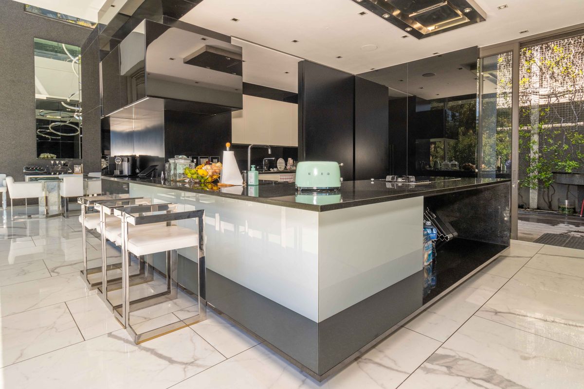 Modern open-plan kitchen featuring a large central island with stone countertops, high-gloss cabinetry, integrated appliances, and polished marble-style flooring.