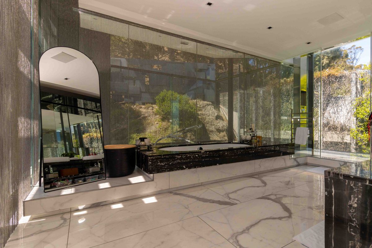 Luxurious modern bathroom featuring a built-in soaking tub, marble flooring, and floor-to-ceiling glass walls overlooking a private garden.