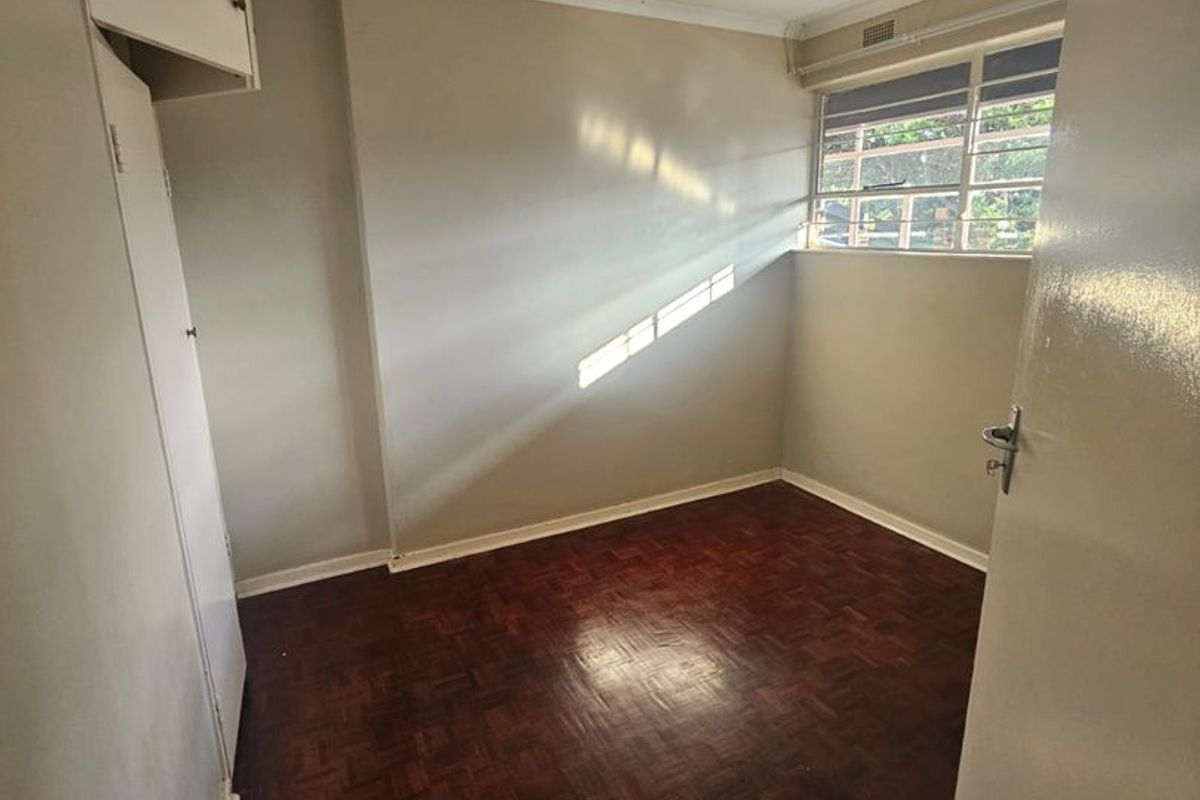 A vacant bedroom featuring original parquet flooring, built-in cupboards, and a large window providing natural light.