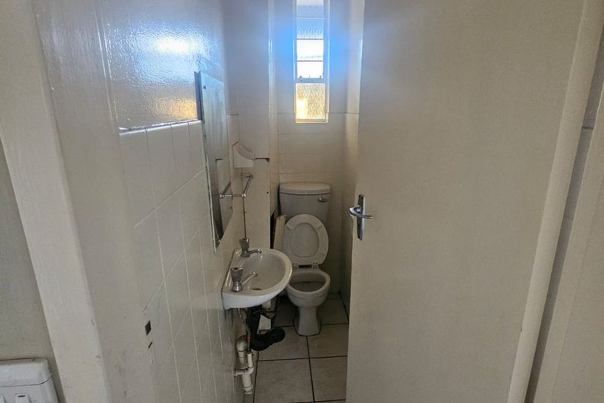 A compact, functional guest bathroom featuring a wall-mounted basin, toilet, and tiled finishes, requiring cosmetic updates.