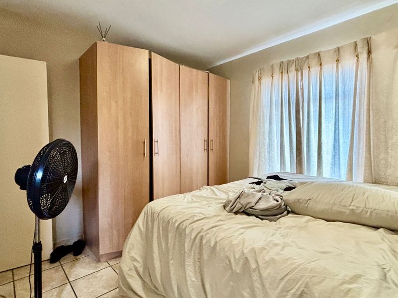 A functional bedroom featuring neutral wall tones, tiled flooring, and a large built-in wardrobe providing ample storage space.