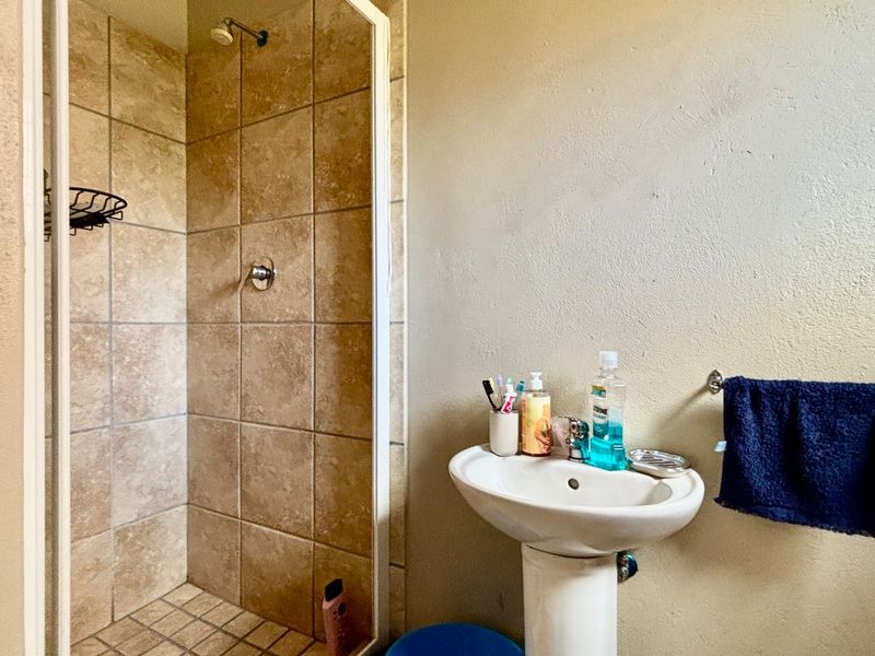 A functional bathroom featuring a pedestal basin and a tiled shower enclosure with a glass door.