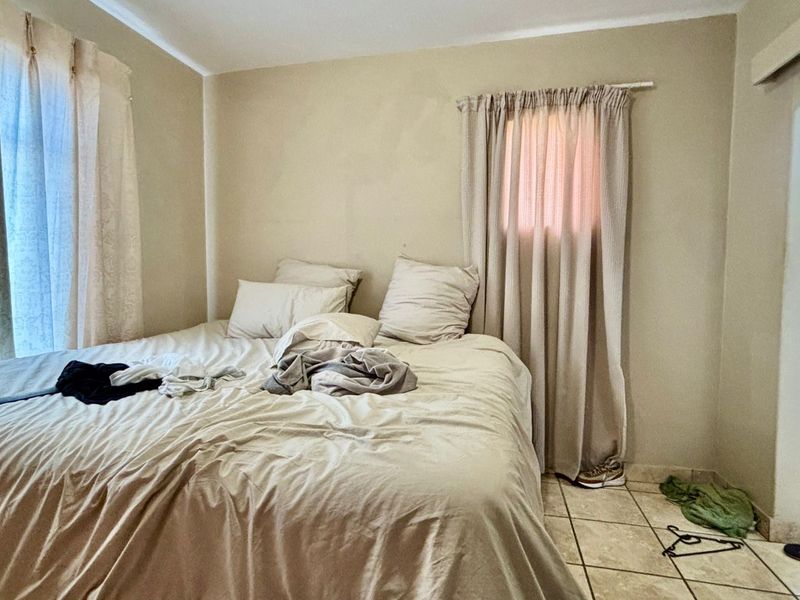 A bedroom featuring tiled flooring and neutral wall tones, with an adjoining bathroom visible through the doorway.