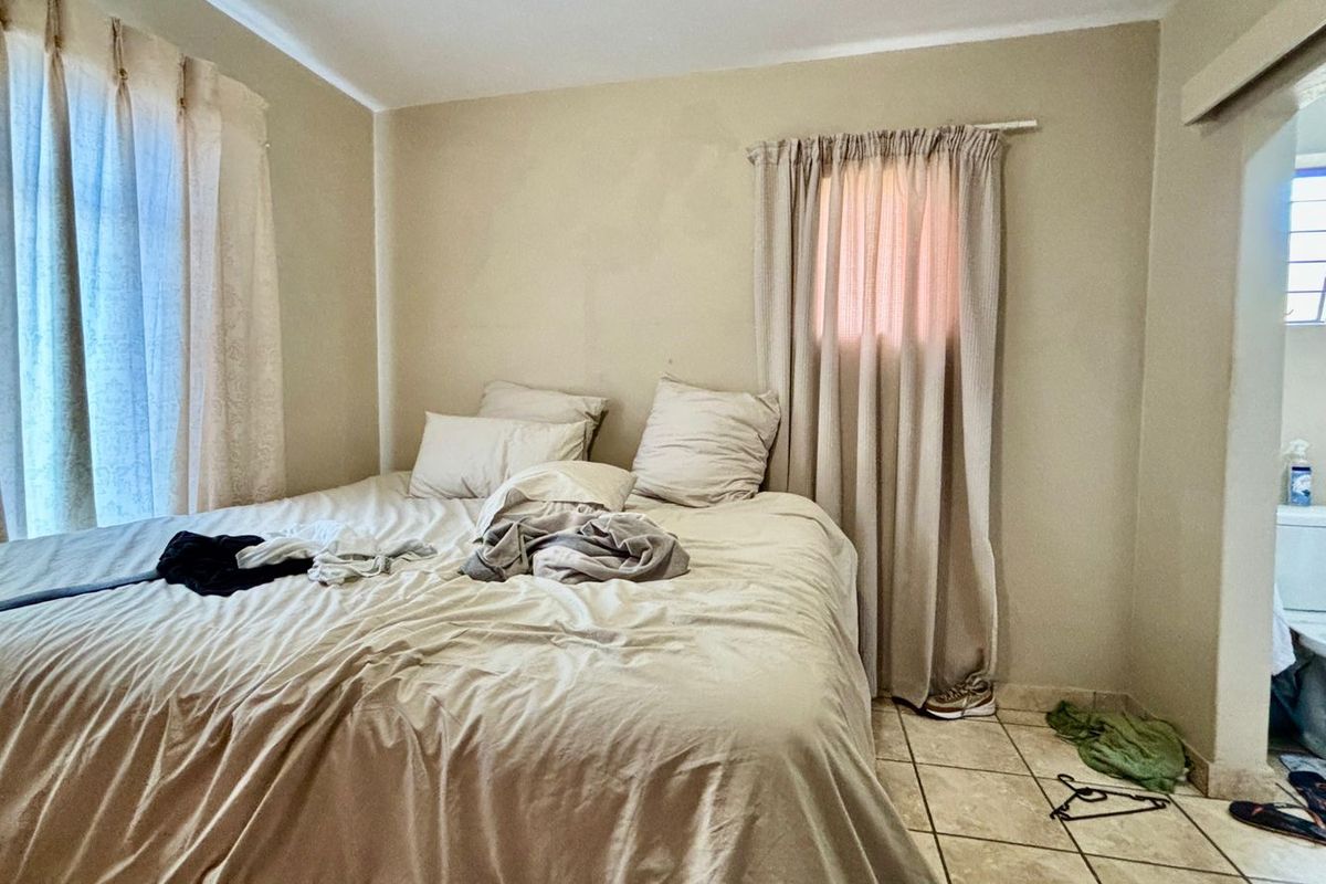 A bedroom featuring tiled flooring and neutral wall tones, with an adjoining bathroom visible through the doorway.