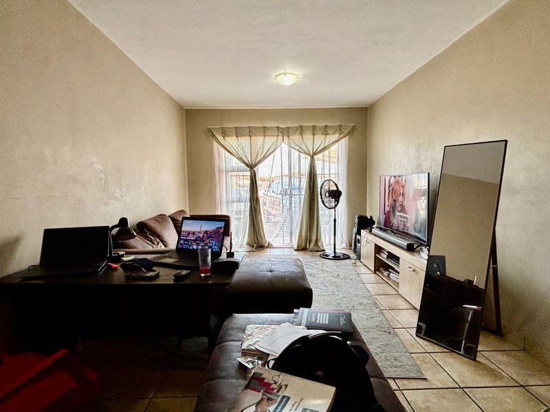 A living room featuring tiled flooring and a sliding glass door leading to an outdoor area, with walls showing signs of wear.