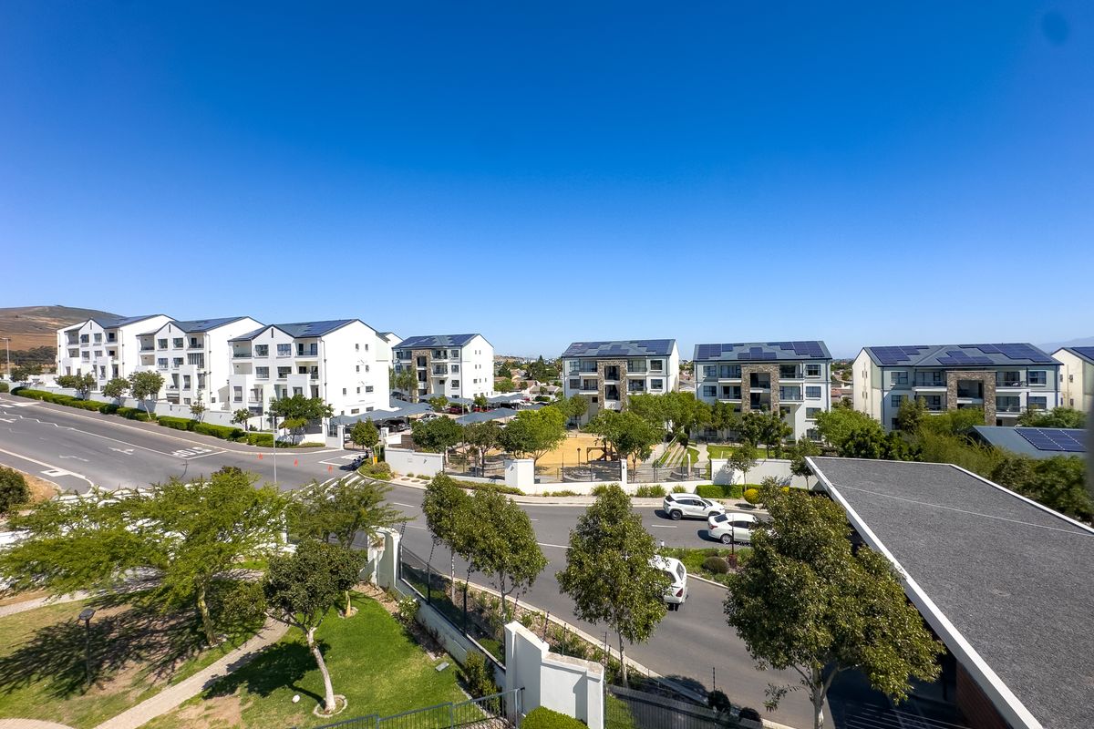 An elevated aerial view of a modern apartment complex featuring multiple residential buildings with solar panels, landscaped grounds, and surrounding street infrastructure.
