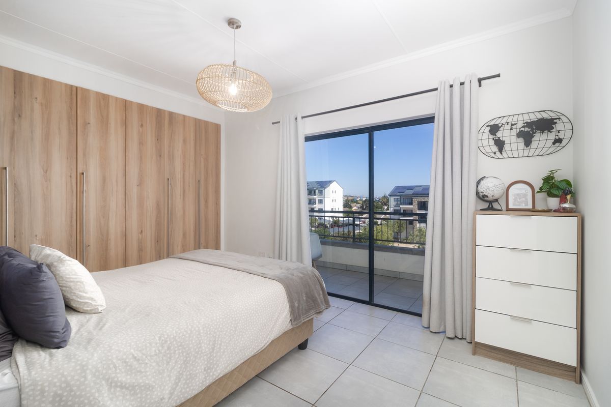 A bright bedroom featuring built-in wood-finish wardrobes, tiled flooring, and sliding glass doors that open onto a private balcony.