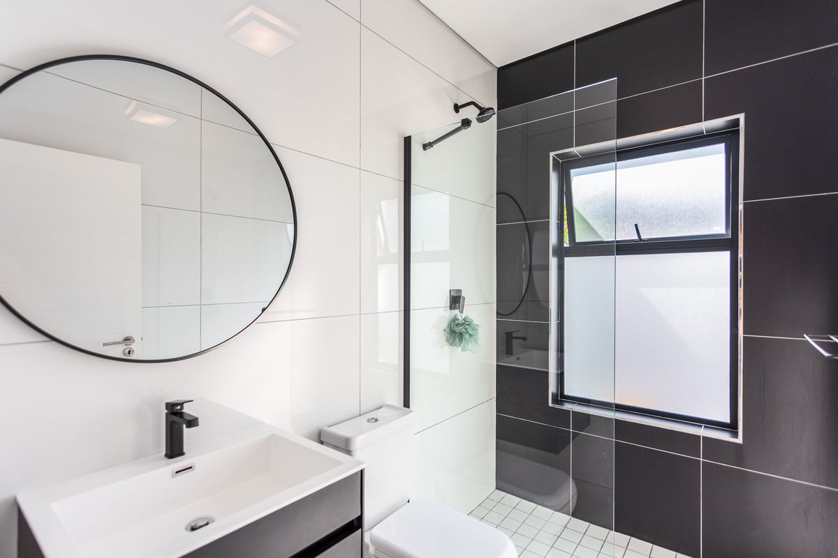 Modern bathroom featuring a sleek vanity, black fixtures, a walk-in shower with glass screen, and contrasting white and black wall tiling.