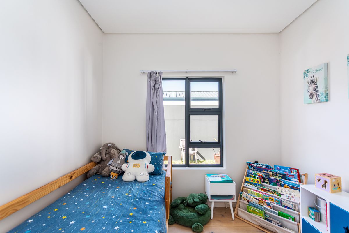 A bright bedroom featuring neutral walls, timber-look flooring, and a modern dark-framed window providing natural light.