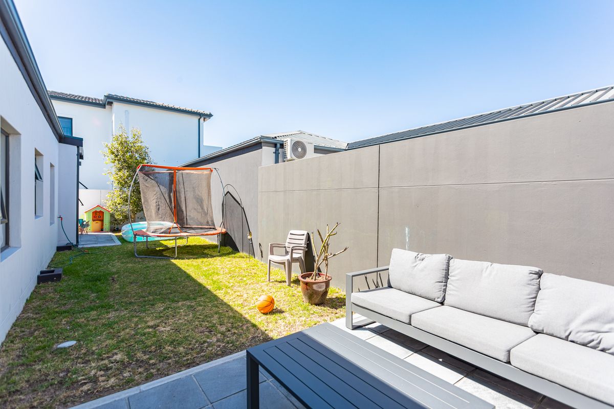 A private rear garden featuring a paved patio area, a small lawn, and high boundary walls for added privacy.