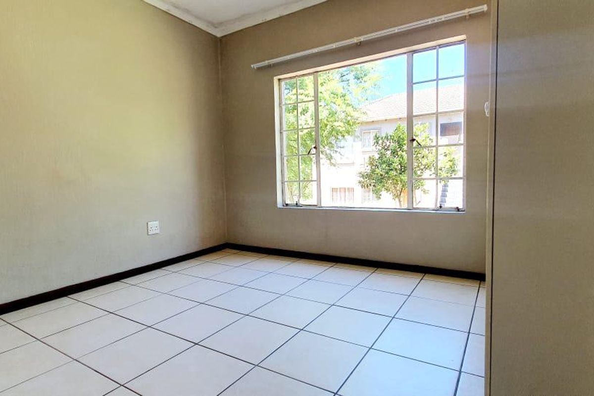 A bright, empty bedroom featuring neutral tiled flooring, a large window providing natural light, and a built-in cupboard.