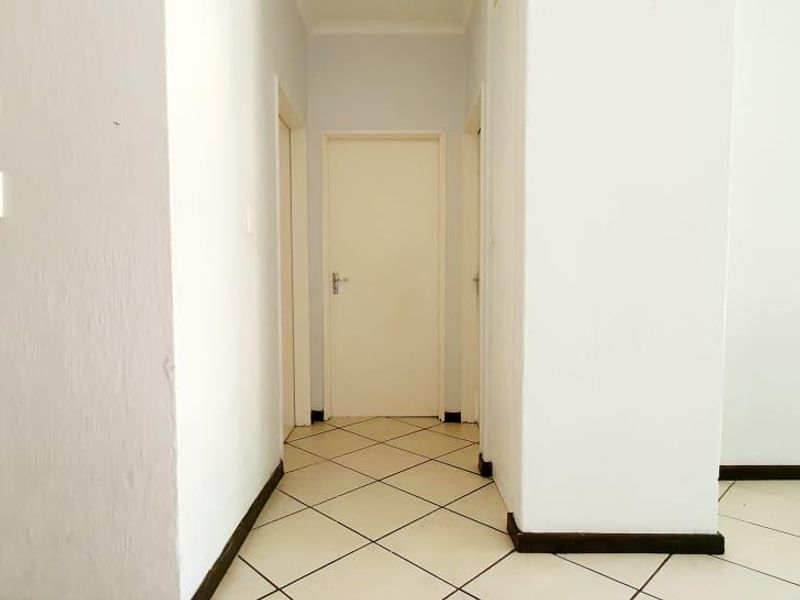 A clean, empty hallway featuring neutral tiled flooring and multiple internal doors, providing access to various rooms within the apartment.