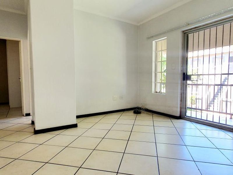 An empty, open-plan living area featuring tiled flooring and a large sliding glass door with security bars, providing access to the exterior.