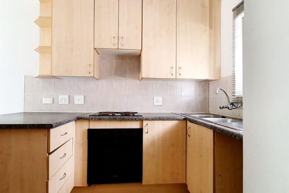 A functional kitchen featuring light wood cabinetry, granite-look laminate countertops, a built-in oven and hob, and a double sink with tiled backsplash.