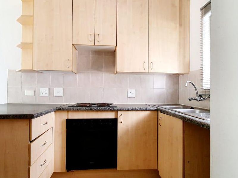 A functional kitchen featuring light wood cabinetry, granite-look laminate countertops, a built-in oven and hob, and a double sink with tiled backsplash.