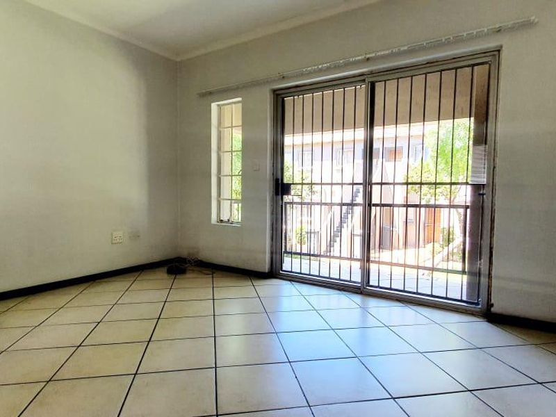 An empty living room featuring tiled flooring and a sliding glass door with a security gate, providing access to the exterior.