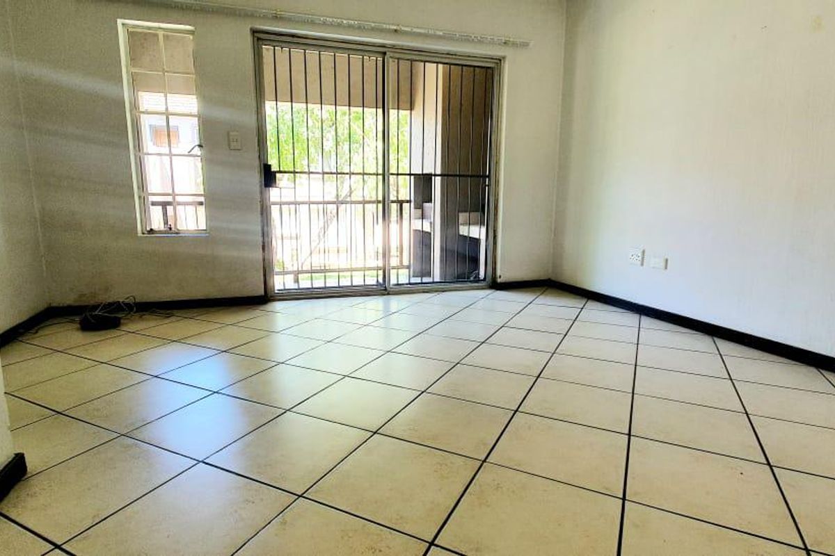 An empty living room featuring tiled flooring, a sliding glass door with security gate, and access to an outdoor area.