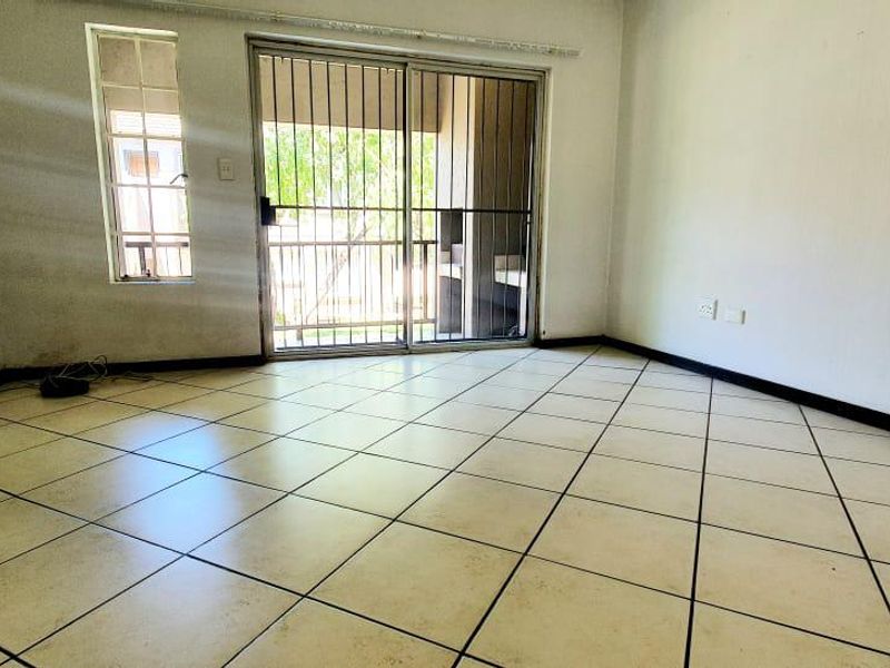 An empty living room featuring tiled flooring, a sliding glass door with security gate, and access to an outdoor area.