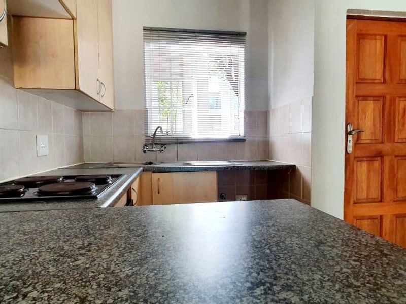 A functional kitchen featuring laminate cabinetry, granite countertops, an electric hob, and a tiled splashback, with a timber door leading to the exterior.