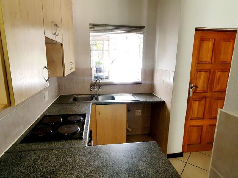A functional kitchen featuring built-in cabinetry, laminate countertops, an electric hob, and a double bowl sink with tiled backsplash and flooring.