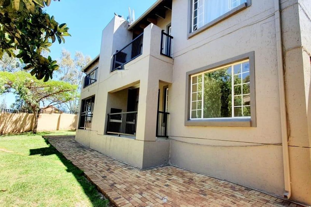 Rear view of the apartment building featuring paved walkways, balconies with metal railings, and established garden space.