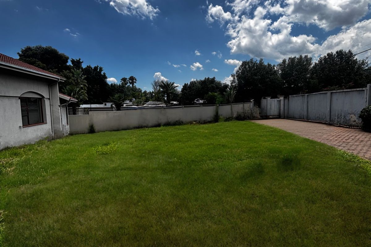 A spacious rear garden featuring a well-maintained lawn, perimeter boundary walls, and a paved driveway area extending from the side of the house.