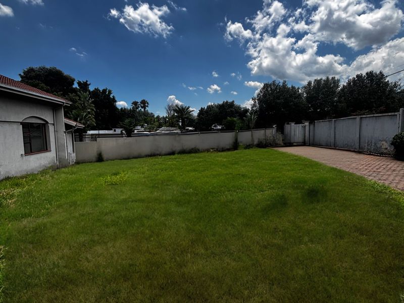 A spacious rear garden featuring a well-maintained lawn, perimeter boundary walls, and a paved driveway area extending from the side of the house.