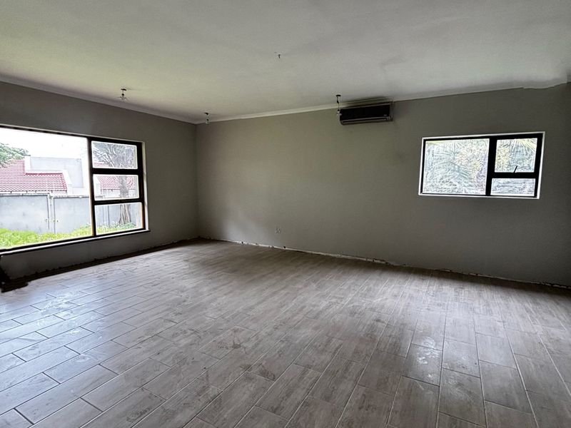A spacious, empty living area featuring wood-look tiled flooring, aluminium-framed windows, and a wall-mounted air conditioning unit, ready for personalization.