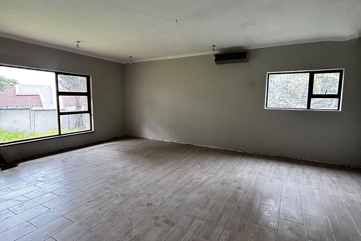 A spacious, empty living area featuring wood-look tiled flooring, aluminium-framed windows, and a wall-mounted air conditioning unit, ready for personalization.
