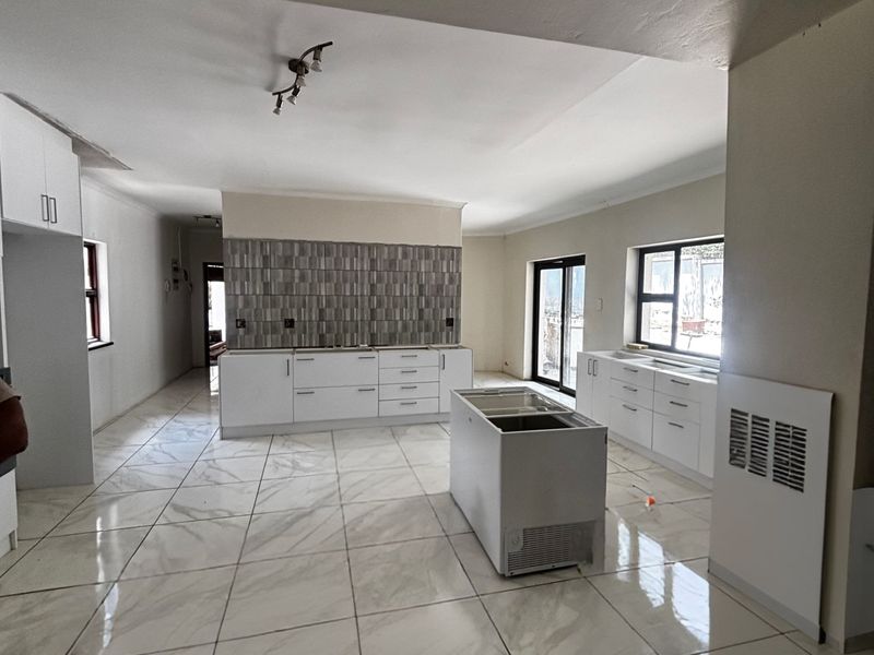 Spacious open-plan kitchen area featuring modern white cabinetry, large format floor tiles, and a central island, currently in an unfinished state.